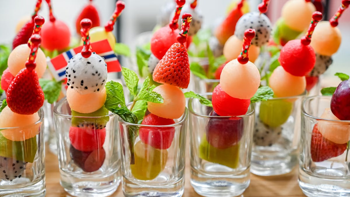 Vibrant fruit skewers in shot glasses with strawberries, dragon fruit, and mint leaves.